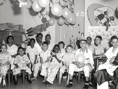 Historic photograph of pediatric patients and staff gathered in a children’s hospital room at UTMB.