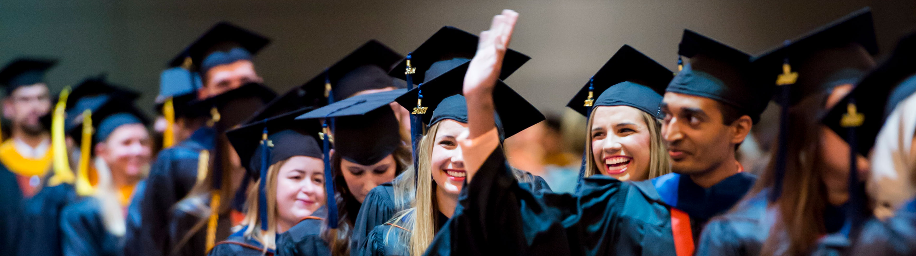 Graduate raising his hand greeting family and friends in the stands