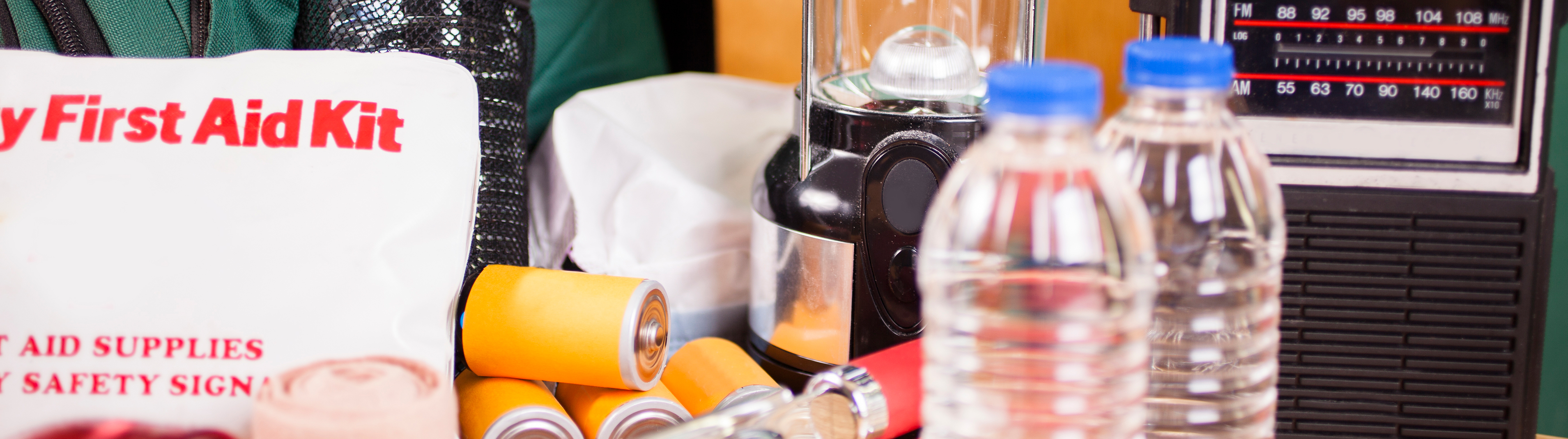 Close up image of items needed to survive an emergency situation like a flashlight, water, batteries and a radio.