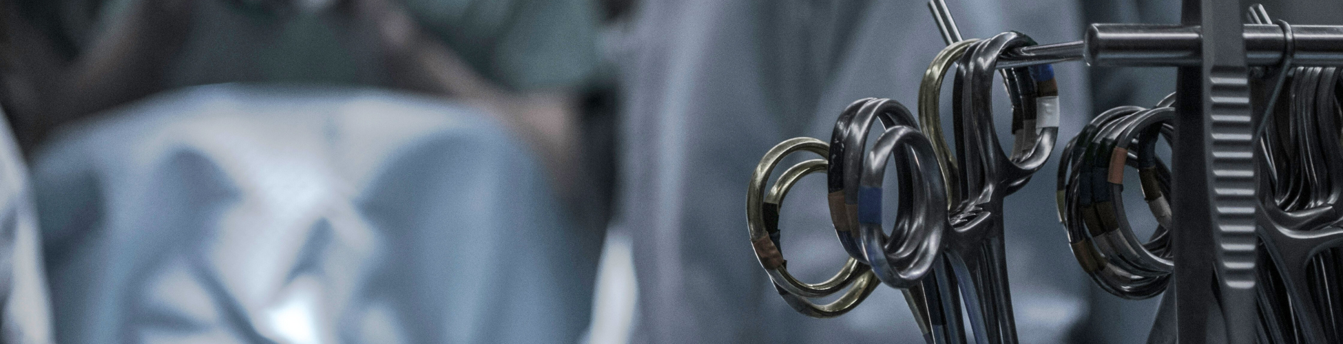 Close-up of surgical instrument finger rings hanging on a metal rack with a blurred operating room setting in the background.