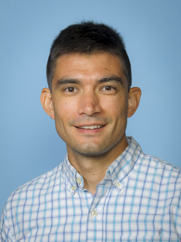 Professional headshot of an individual wearing a light-colored patterned blouse against a solid blue background.