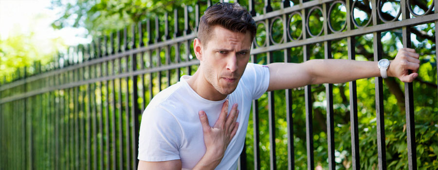Out-of-breath man with hand on chest, leaning against fence
