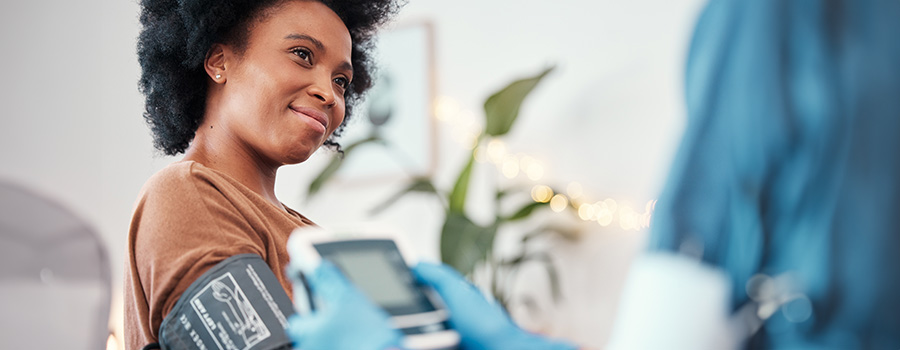 A woman smiles while a UTMB healthcare professional checks her blood pressure.