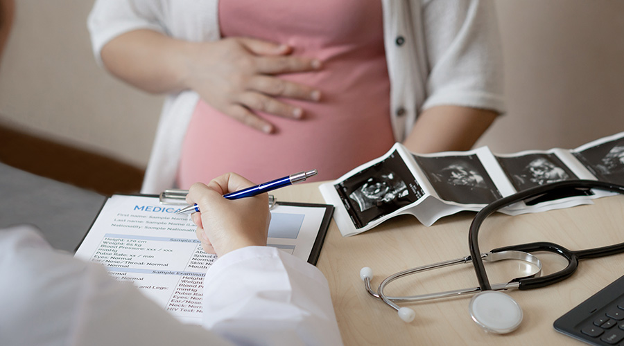 A pregnant woman holds her belly while talking with a UTMB Health provider reviewing ultrasound images.