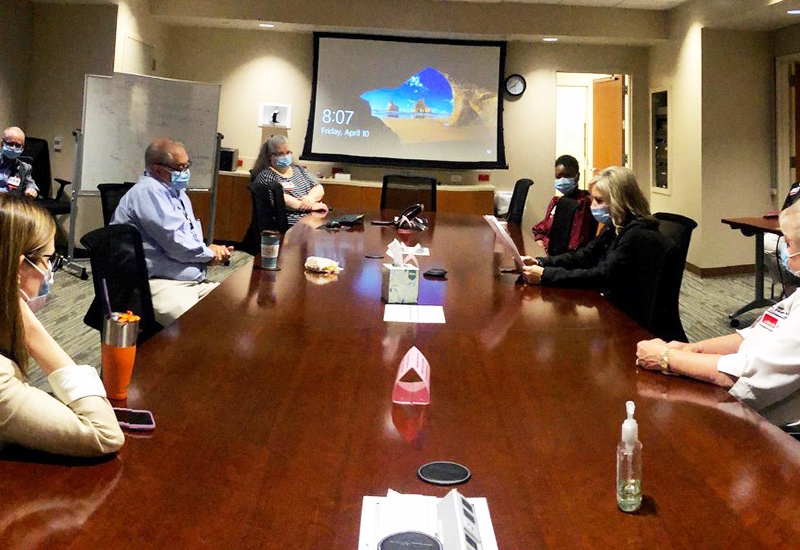 Staff seated around a conference table during a meeting, with a screen displaying a desktop background and masks worn by participants.