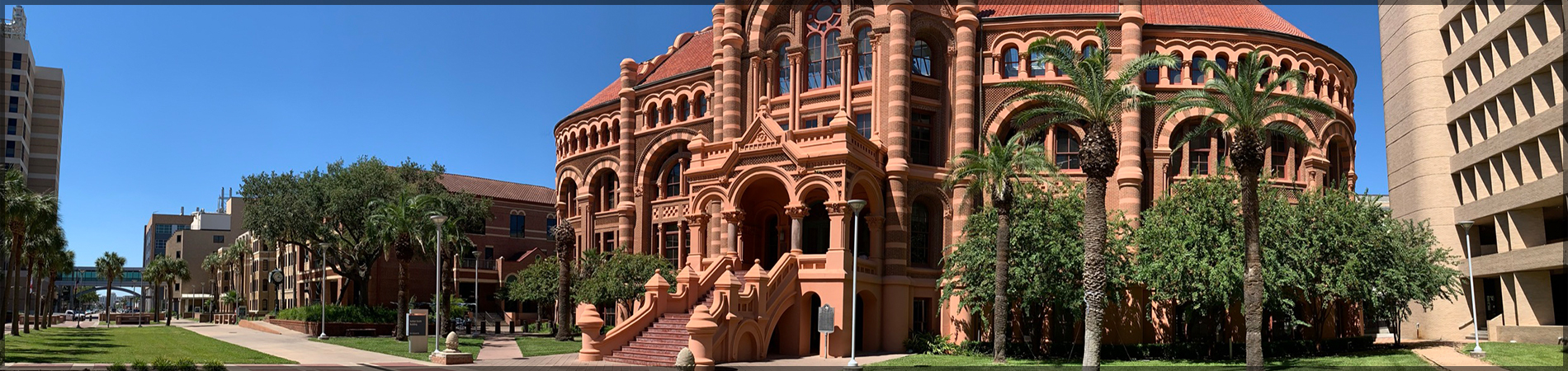Historic red-brick UTMB building with arched windows, grand staircase, and palm trees on a sunny campus walkway
