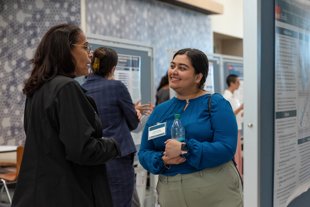 A professor speaks with an MD-MPH student about her poster at the 2025 Public Health Symposium