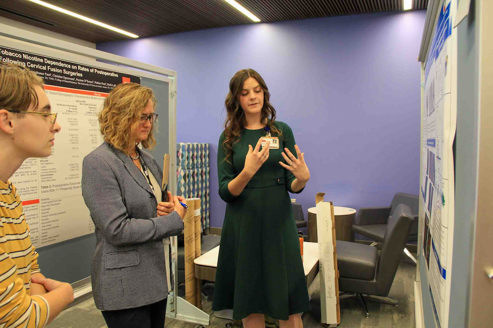 A student explains a research poster to faculty and another attendee during a doctoral program event.
